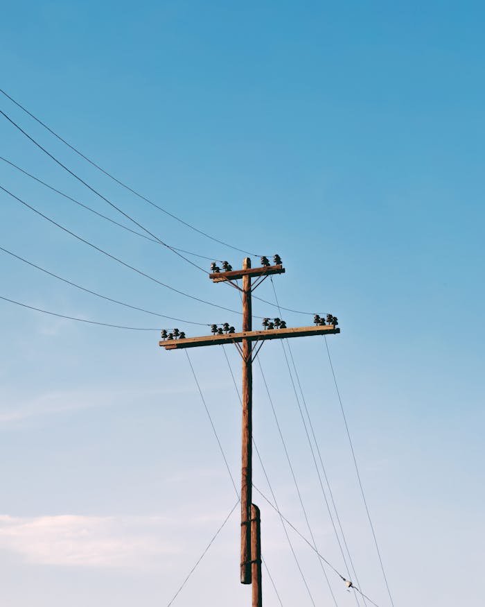 Electrical pole with power lines under a clear blue sky, minimal clouds.